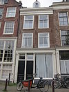 Huis met latere gevel onder rechte lijst waarop een dakkapel in het op het voorste deel van het huis geplaatste dwarse dak