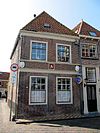 Pand met van top beroofde 17e-eeuwse gevel met drie gevelstenen in het Fries