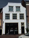 Pand met brede afgeknotte klokgevel, gepleisterd, beneden verbouwd