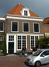 Pand met lijstgevel, horizontale hardstenen band, fraai gebeeldhouwde Louis seize deur