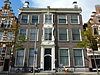 Statig patriciershuis, hoge gevel met rechte kroonlijst, versierde middenpartij, fraaie vaasvormige natuurstenen schoorstenen. Fraai gesmeed régence stoephek verdwenen