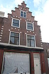 Pand met trapgevel in haarlemse trant, natuursteen versieringen, blokken aan bogen en randen, toppinakel rustend op console boven kruisvenster