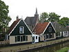 Pand onder zadeldak; houten geveltopbeschietingen, aan de voorzijde met gesneden windveren. Gepleisterde gevel