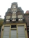 Hoekpand Noordzijde Roode Steen. Huis met verhoogde halsgevel met twee pilasters opgaande van de puibalk en doorlopend langs de hals. Festoen, oeil de boeuf-omlijstingen, gevelsteen en jaartalsteen