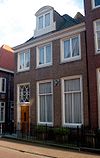 Eenvoudig pand, met rechte gootlijst en dakkapel. Stoep met eenvoudig hek
