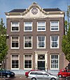 Vier traveeën breed pand met twee verdiepingen, bekroond door verhoogde gootlijst met rococo-snijwerk. Pui garage. Inwendig betimmering en schouw van stucwerk
