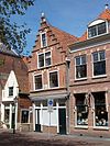 Gaaf pand met hoge trapgevel; verdieping overgekraagd in de Schoolsteeg; gevelsteen: In de kolfstok