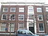 Zeer brede panden, waarvan het linker een gevel heeft door gladde pilasters en een middenrisaliet geleed; deurpartij met rococo-snijwerk. Rechter pand niet geleed; snijwerk aan deuromlijsting en kroonlijst