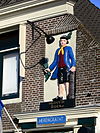 WLM - M.arjon - Muiden Herengracht 71 (1) - Joost Middendorp verkocht in 1697 tabak in dit pand. Op de gevelsteen staat een boer uit het Gooi. Hij heeft in zijn rechterhand een tabaksblad en zijn andere hand rust op een rol tabak. De steen dateert vermoedelijk uit 1756, toen de toenmalige eigenaar, Bruyn Schuylenburg, het pand liet verbouwen. De steen was bedoeld als herkenningsteken, zodat men kon zien dat hier tabak verkocht werd. Dat was in die tijd heel gebruikelijk. Men toonde het beroep of het ambacht door middel van gevelversierin…