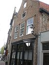Huis met gepleisterde klokgevel, de top half cirkelvormig met natuursteen afgedekt