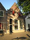 Achter de Muren Vispoort 16 v02.JPG -  Achter de Muren Vispoort 16, Deventer, The Netherlands is national heritage: a warehouse with gable roof with plastered wall spout. Stone profiled weatherboards on shoulders and top. Arched attic and loft hatches, hoist anchor. Ground floor altered.  Achter de Muren Vispoort 16, Deventer, Nederland is een rijksmonument: een pakhuis onder zadeldak met gepleisterde tuitgevel. Geprofileerde natuurstenen dekstukken op schouders en top. Getoogde zolder- en vlieringluiken; hijsankers. Beganegrond ge…