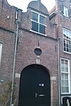 Huis met in- en uitgezwenkte topgevel voorzien van drie pinakels, gedekt door geprofileerde natuurstenen platen