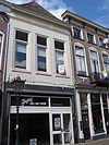 Huis met geverfde lijstgevel met lijst met tandlijst en met jongere winkelpui