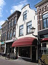 Huis met geverfde in- en uitgezwenkte topgevel, siersteen en jongere winkelpui