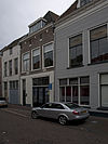 Pand met gepleisterde pui met boven de vensters van de verdieping restanten van ontlastingsbogen met muurankers
