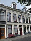 Pand met gepleisterde lijstgevel onder verminkt zadeldak