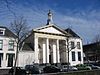 Kampen Lutherse Kerk op de Burgwal.JPG -  Kampen - Lutherse Kerk - LUTHERSE KERK. Gebouw op rechthoekige grondslag; aan de Burgwal gepleisterde neo-klassicistische gevel met zuilen, dorische kroonlijst met fronton over de gehele gevelbreedte; bekroning in de vorm van rond koepeltorentje met zwaan 