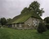 Overzicht van de voorgevel en de linkerzijgevel van de boerderij met rieten dak
