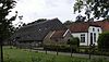 Boerderij bestaande uit een schuur onder rieten wolfdak, waarvoor een woonhuis is aangebouwd met gepleisterde wanden, een ingezwenkt lijstgeveltje en een met pannen gedekt dak, alsmede het bakhuis