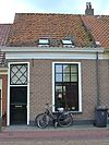 Eenvoudig pand onder zadeldak met deur met bovenlicht en vensters met roedenverdeling, achter gevel met nr. 51
