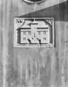 Huis met gepleisterde gevel met rechte kroonlijst, in het midden dakkapel met plat dak, de kroonlijst doorsnijdend. Gebeeldhouwde steen met afbeelding van het huis 