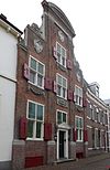 Huis met zware halsgevel met bakstenen pilasters; gebeeldhouwde natuurstenen vleugelstukken, gebeeldhouwde guirlandes en cartouches