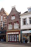 Huis met eenvoudige halsgevel, onder tot winkel verbouwd. Van belang voor nr 45