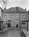 Huis met witgepleisterde gevel. Stoeppalen met kettingen