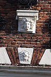 Huis met trapgevel, met mozaiekwerk, sierankers en maskers, bekroond door schilddragende leeuw. Achterzijde eenvoudige topgevel van vroeger datum