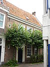 Huis met zakgoot, dubbel zadeldak en rechte kroonlijst. In de singel uitgebouwd tuinhuis. Aan de korte zijde dubbele topgevel met littekens van oudere gevel