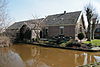 Vinkeveen, Demmerik 55, langhuisboerderij, noordzijde -img0382 -  Landhuisboerderij met aan de waterkant een aangebouwd boenhok. Een boenhok had een werkstoep direct aan het water gelegen en kon met een luik worden afgesloten. Op de werkstoep werden de melkbussen en â€“emmers met helder slootwater schoongemaakt. Het boenhok had ook een huishoudelijke functie. Meestal stond er in het boenhok een waterfornuis voor het koken van de was en/of het koken van aardappels voor de varkens. Ook voor de kaasmakerij was warm water nodig. 