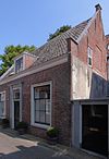 Laag huis met rechte kroonlijst, zadeldaken eindigend in dubbele topgevels