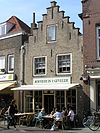 Huis met trapgevel. Geprofileerde dekplaten en overhoekse toppilaster. Boven de vensters ontlastingsbogen. Staafankers. winkelpui
