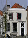 Huis met gepleisterde ingezwenkte lijstgevel. Voordeuromlijsting met verdiepte posten. Staafankers