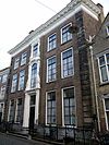 Huis met deftige lijstgevel op voet van natuursteen met zwartgeverfde banden en aan weerszijden afgezet door natuurstenen blokpilasters