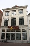 Pand met verdieping, zolderverdieping en schilddak. Gepleisterde gevel onder rechte houten kroonlijst. Winkelpui