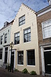 Huis met gecementeerde trapgevel. De treden afgedekt met natuurstenen platen. Voordeuromlijsting met bovenlicht (Huis verplaatst vanaf de Dam naar huidige locatie)