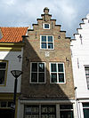Huis met gepleisterde trapgevel. De treden afgedekt met natuurstenen platen. Moderne winkelpui