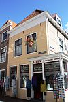 Huis met gepleisterde lijstgevel. Dakkapel. Piron. Zijgevel met uitbouw oorspronkelijk pothuis, aan de zijde van de Lepelstraat. Winkelpui