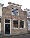 Huis met ingezwenkte gevel onder de lijst gepleisterd, met stoep met stoeppaal