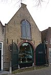 Stalgebouw met gepleisterde puntgevel. Getoogde poort en zoldervensters. Stoeppaal