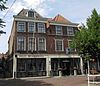 Hoekpand Schoolstraat. Pand onder omlopend schilddak; achterhuis onder schilddak evenwijdig aan de Schoolstraat. Eenvoudige lijstgevel met in het fries verdiepte velden. Geprofileerde vensterdorpels