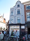 Ondiep pand op de hoek van het verbindingsstraatje tussen Markt en O. Langendijk. Gepleisterde voorgevel, waarvan het rechterdeel hoger is opgehaald en beëindigd als klokgevel onder rollaag