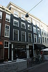 Breed pand met lijstgevel - in het fries van de lijst gesneden versieringen - onderpui in tweeën gewijzigd
