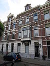 Pand met neo-renaissancegevel. De parterre heeft in pleister uitgevoerd bossagewerk. Ontlastingsbogen met vlechtwerk in de boogtrommels. Erker