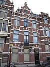 Pand in neo-renaissance trant met trapgevel boven de middenas. De gevel is versierd met geblokte ontlastingsbogen en banden