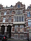 Pand in neo-renaissance trant met rechts topgevel. Brede houten erker op korbelen. Gevelversiering met banden en blokken. Links getoogde ingangspartij