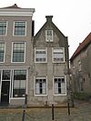 Hoekpand met zadeldak tussen puntgevels, waarvan de voorgevel gepleisterd. Stoep met stoeppaal