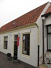 Gepleisterd dwarshuis onder zadeldak. Ramen en deuren (met gietijzeren bovenlichten) uit de bouwtijd. Onder een dak met het buurnummer 24
