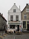 Hoekpand met zadeldak tussen puntgevels. De gepleisterde voorgevel heeft onder de top een waterlijst en in de verdieping Empireramen. Stoep met houten palen